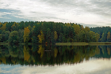 Fototapeta na wymiar Autumn landscape. Forest on the shore of the lake .. Reflection in the water. The beginning of leaf fall.