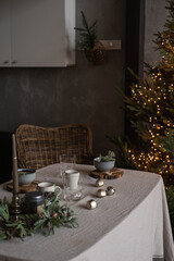 Modern home interior design. Comfortable cozy living room decorated with Christmas tree, rattan chair, table with linen cloth. Christmas, New Year holidays celebration dinner