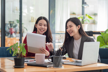 Fototapeta na wymiar Two casual Asian businesswomen discussing work in the office