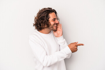 Young caucasian man isolated on gray background saying a gossip, pointing to side reporting...