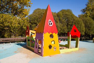 Wooden fairy-tale houses of unusual shape in red and yellow with a sandbox on a background of green trees on a clear sunny day. Playgrounds, sports, health entertainment.