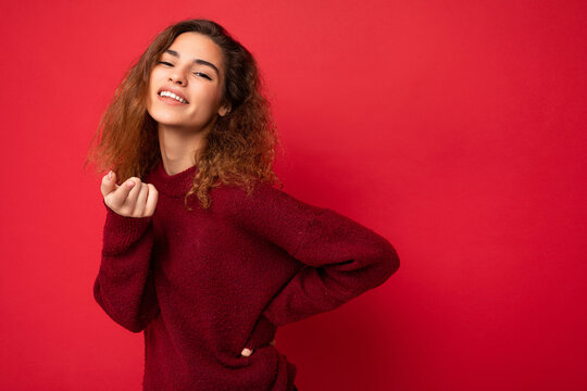 Portrait of young positive happy attractive brunette curly woman with sincere emotions wearing casual red sweater isolated on red background with copy space