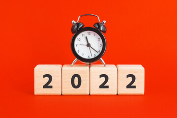 Wooden cubes with 2022 and mini alarm clock on red background. New year, time concept. Square blocks.