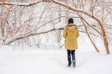 Fototapeta na wymiar A teenage girl walks in a winter forest. Back view of a girl in a green coat standing in the snow