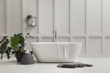 Naklejka na ściany i meble Modern ceramic bathtub and green plant near white wall indoors