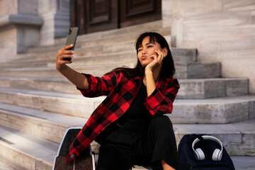 Portrait of young beautiful girl with skateboard. Happy smiling woman taking selfie photo..