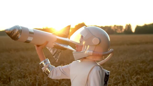 Little young happy cute child boy wearing astronaut uniform and helmet cosmonaut playing, launching toy rocket at sunset field, Space man, Kid dream flying, childhood, freedom, travel, future concept