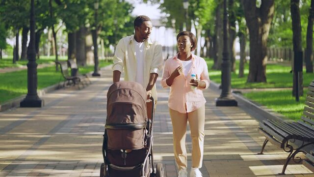 Happy father pushing baby stroller, talking to wife with milk bottle, closeness