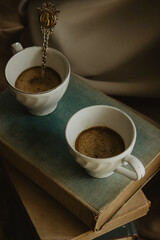 Close-up image of two coffee cups with an original spoon on books on an isolated beige background.