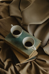 Two coffee cups on top of books on an isolated beige background.