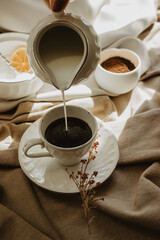 Female hand pours milk into cup of coffee. Still Life oh hot coffee on brown background.