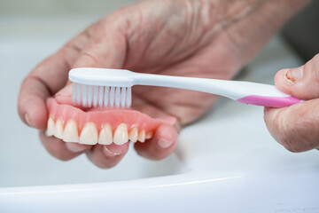 Asian senior or elderly old woman patient use toothbrush to clean partial denture of replacement...