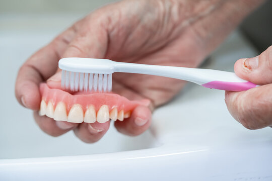 Asian senior or elderly old woman patient use toothbrush to clean partial denture of replacement teeth.