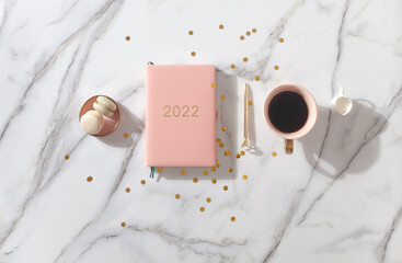 Pink coral colored diary for the year 2022, pen, coffee, macaron cookie. Marble background