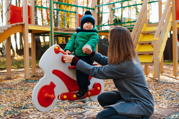 Young mother with child playing on playground, mom holding hand of laughing cheerful baby kid...