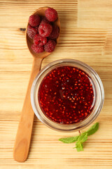 Glass bowl of raspberry jam with ingredients on wooden background