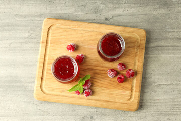 Glass jars of raspberry jam with ingredients on wooden board