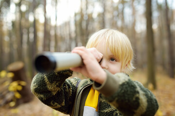 Little boy scout with spyglass during hiking in autumn forest. Child is looking through a spyglass. Concepts of adventure, scouting and hiking tourism for kids.