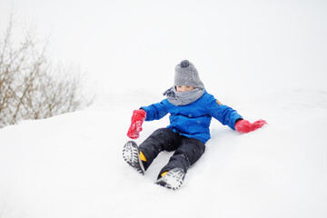 Fototapeta na wymiar Little boy enjoy riding on ice slide on snowy day. Baby having fun during blizzard. Outdoor winter activities for kids.