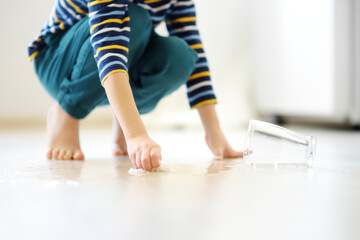 Little boy wipes water spilled from a glass on the floor. Teaching a child to clean up after himself. Responsibility, accuracy.