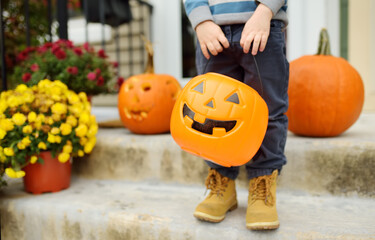 Little boy at halloween celebrations party. Child holds a bucket shaped like a halloween pumpkin...