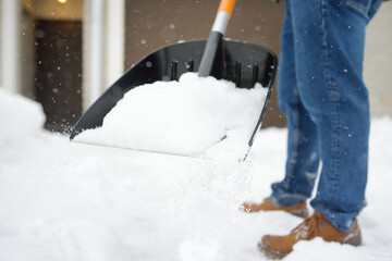 A mature man clean path near house from snow during strong blizzard. Person shoveling snow out of the driveway. Huge snowdrifts. Difficult situation in the city after a snow storm