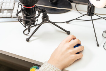 Hand of a young influencer woman holding a mouse with her microphone on the table. Technology, streaming, online and communications concept,