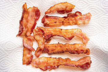 Top view of crispy bacon strips on oil-absorbing tissue paper in many shapes with copy space. Keto...
