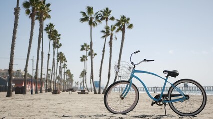 Fototapeta premium Blue bicycle, cruiser bike by sandy ocean beach, pacific coast near Oceanside pier, California USA. Summertime vacations, sea shore. Vintage cycle, tropical palm trees, lifeguard tower watchtower hut