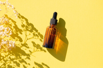 Amber glass dropper bottle with black lid. Top view on yellow background with plant shadow....