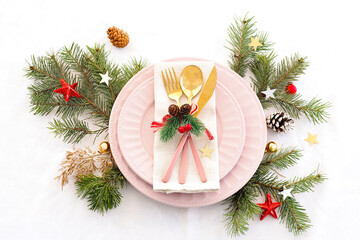 concept of christmas table setting. two pink plates and pink and gold cutlery with decor on a linen napkin. fir branches, cones, balls and stars..