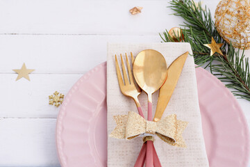 Christmas table setting in white-pink-gold colors. pink plate, cutlery with gold bow, fir branches, snowflakes and stars..