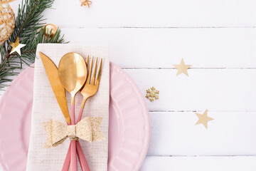 Christmas table setting in white-pink-gold colors. pink plate, cutlery with gold bow, fir branches, snowflakes and stars..