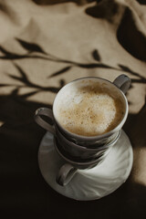Modern coffee cup with milk and foam on a beige background isolated with a plant shadow and a cloth...