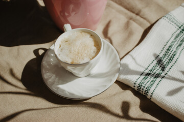 Modern coffee cup with milk and foam on a beige background isolated with a plant shadow and a cloth...
