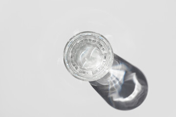 Top view of transparent glass of water with shadow on light background.