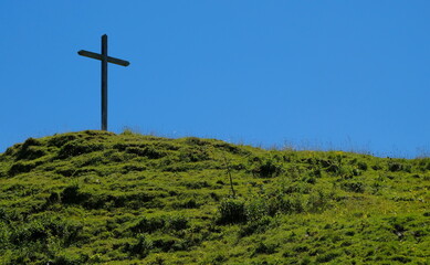 grave hill with a cross with grass against a blue sky