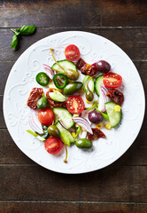 Simple Salad with Green and Kalamata Olives, Cucumber, Cherry and marinated Tomatoes, Capers and Jalapeno Pepper. Dark wooden background. Top view. Close up. 