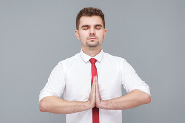 Yoga time. Portrait of young handsome calm man in white shirt and tie standing in yoga pose and try...
