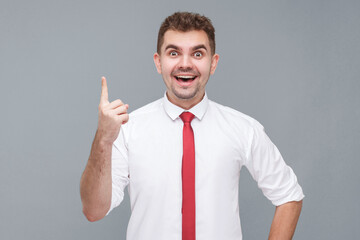 Idea. Portrait of young handsome surprised man in white shirt and tie standing, finger up and looking at camera with idea gesture and enjoy. indoor isolated on gray background.