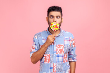 Young adult bearded man wearing blue casual shirt covering his astonished face with round sweet...