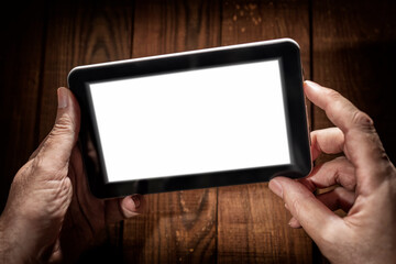 Hands holding tablet with white screen on a wooden background.