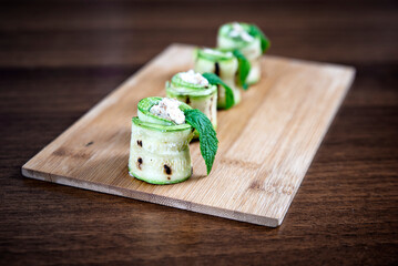 Grilled zucchini rolls with goat cheese on wooden plate