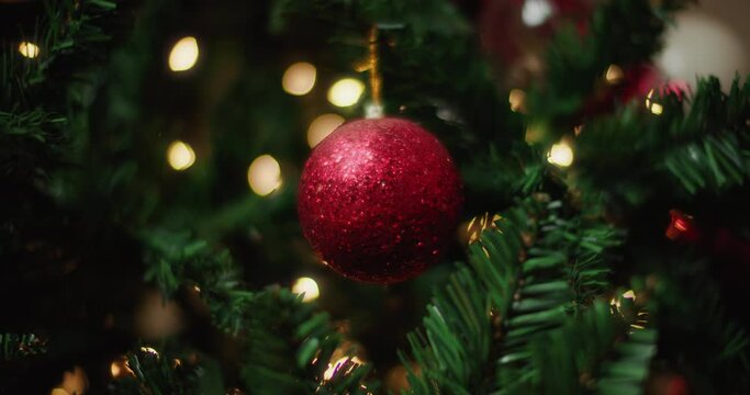 Red glittering ball hanging on a Christmas tree, changing lights in background. Close up, slow motion. 