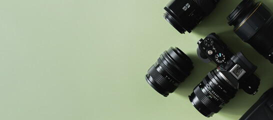 Photographer's or videographer equipment, composition of a camera and lenses on a green background, flat lay. Mock up with space for text, top view. Banner format.