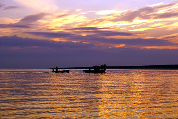 Silhouettes of boats with fishermen fishing at dusk sunset