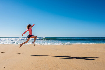 Fototapeta na wymiar cute young girl running and jumping on sunny beach