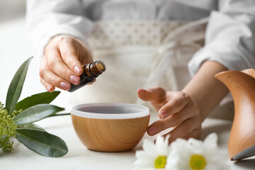 Obraz na płótnie Canvas Woman adding essential oil to aroma diffuser on table