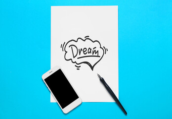Paper with word DREAM, nib pen and mobile phone on blue background