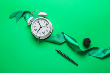 Nib pen with alarm clock, ribbon and ink on green background